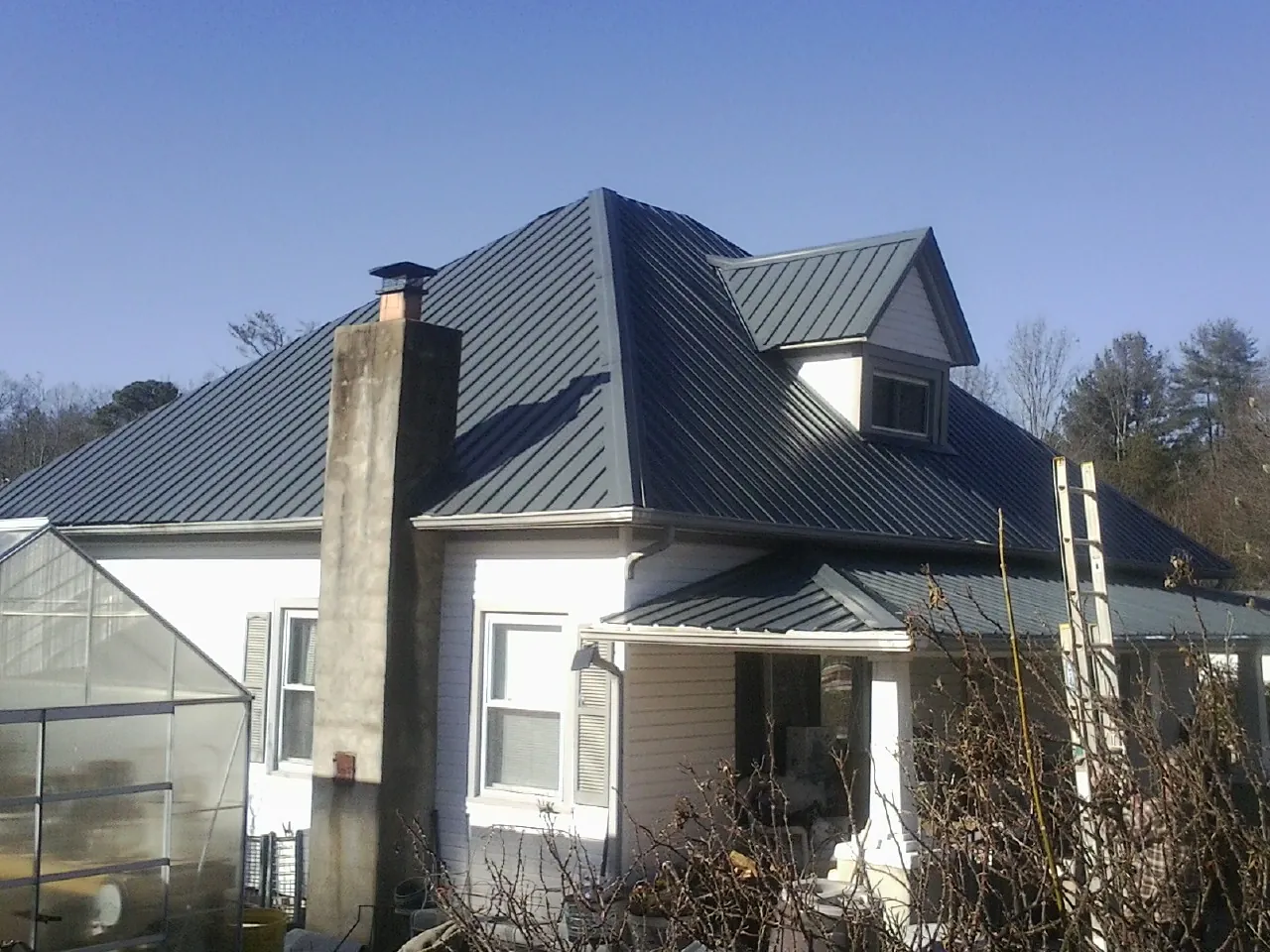 Dark blue standing seam metal roof on a white farmhouse with dormer — Slate & Tile Roof Repair by Roofing Brothers in Newington