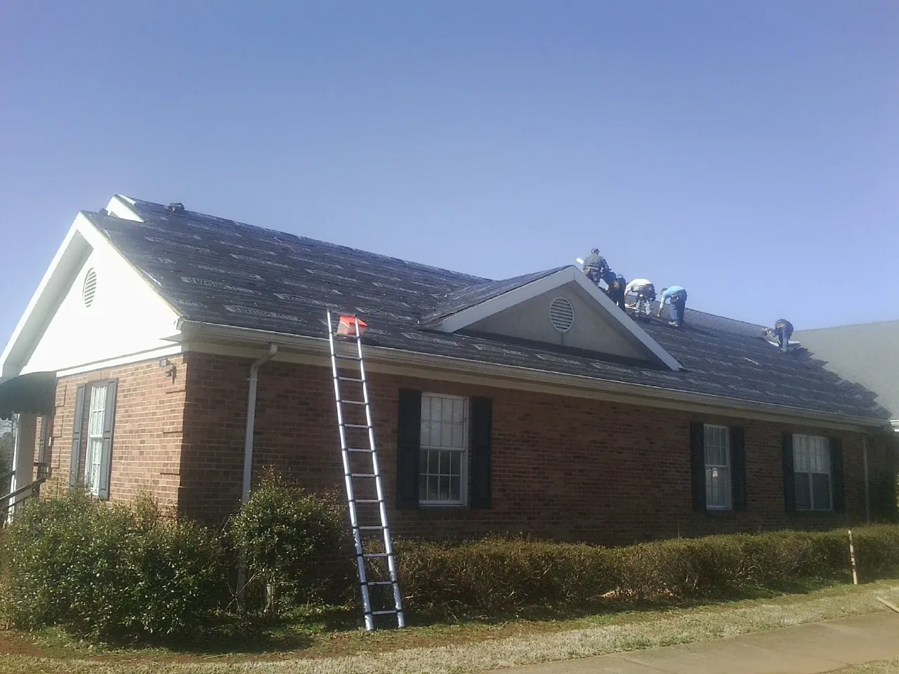 Crew tearing shingles off a brick ranch roof with a ladder set — Emergency Roof Repair work by our crew in Newington