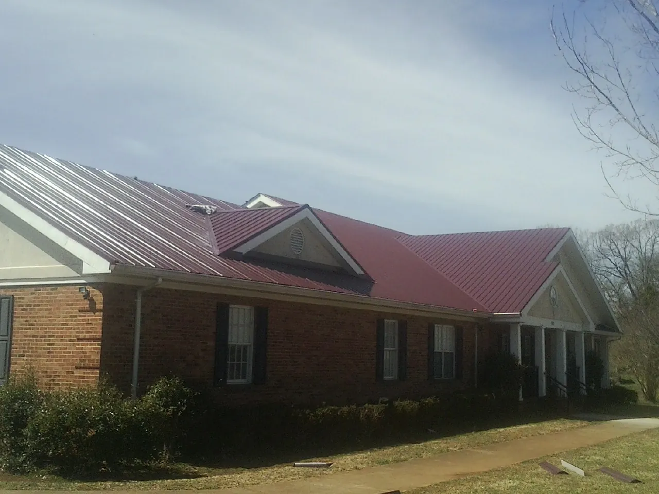 Red metal roof with gabled entries on a long brick building, from a Hail Damage Roof Repair job in Newington